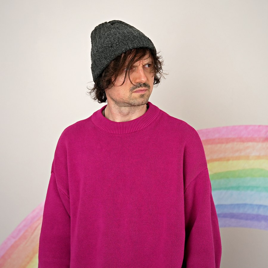 Cedric im pinken Pullover vor einem Regenbogen